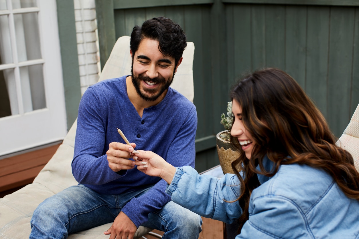 Young couple laughing and smoking a joint together while sitting outside on their patio at home