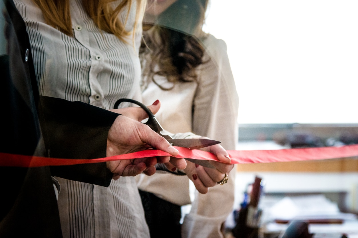 CEO and her assistant cutting a red ribbon, opening ceremony.