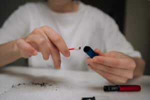 Woman cleaning electronic cigarette mouthpiece with cotton swab, removing residue for hygiene and maintenance in focused, close-up domestic self-care routine.